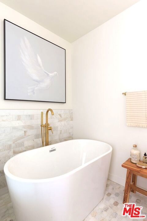 bathroom with a tub to relax in and tile walls