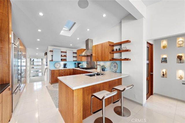 kitchen featuring light tile patterned floors, a kitchen bar, kitchen peninsula, wall chimney exhaust hood, and sink