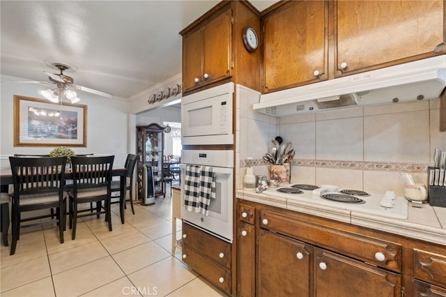 kitchen featuring white appliances, ceiling fan, crown molding, light tile patterned floors, and tile counters