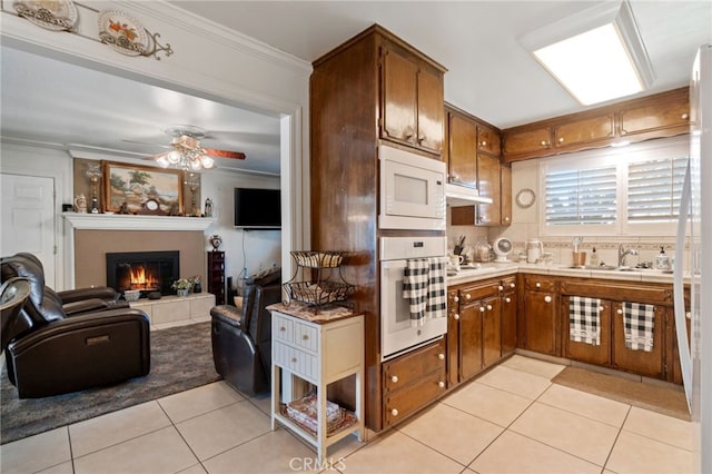 kitchen with a tiled fireplace, sink, light tile patterned flooring, and white appliances