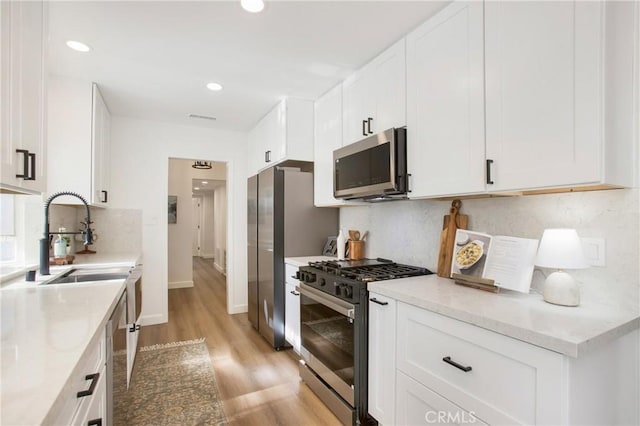 kitchen featuring white cabinets, sink, light hardwood / wood-style flooring, light stone countertops, and appliances with stainless steel finishes