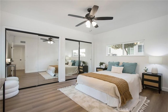 bedroom featuring two closets, ceiling fan, and dark hardwood / wood-style floors