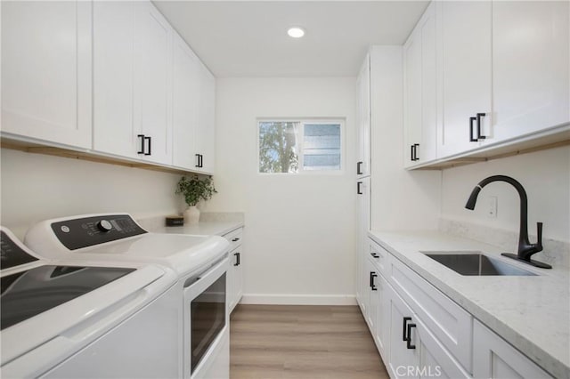 laundry room featuring washing machine and clothes dryer, sink, cabinets, and light hardwood / wood-style flooring