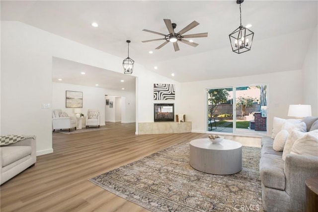 living room with a tiled fireplace, high vaulted ceiling, wood-type flooring, and ceiling fan with notable chandelier