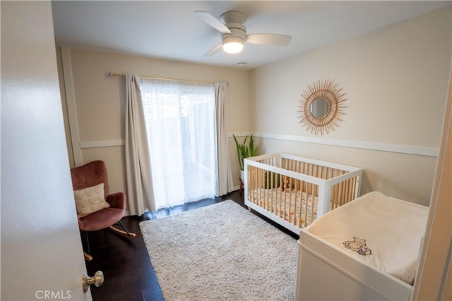 bedroom with a crib, hardwood / wood-style flooring, and ceiling fan