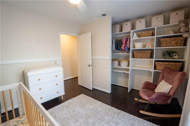 bedroom featuring ceiling fan, a closet, a nursery area, and dark hardwood / wood-style floors