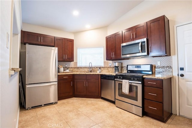 kitchen featuring decorative backsplash, light stone counters, sink, and appliances with stainless steel finishes