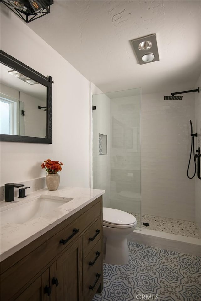 bathroom with a tile shower, vanity, and toilet