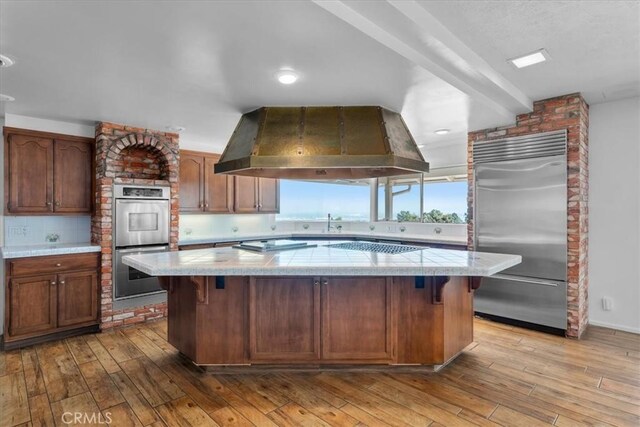 kitchen with light wood-type flooring, stainless steel appliances, a center island, and island exhaust hood