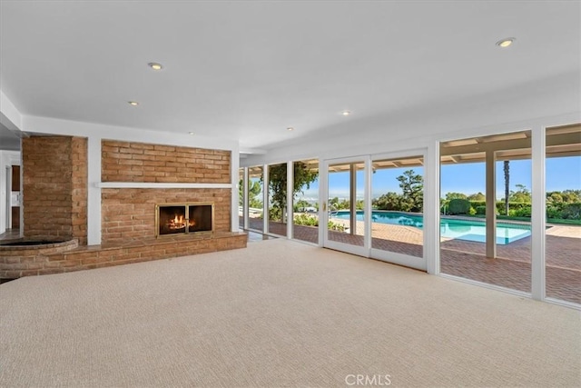 unfurnished living room featuring carpet floors, a brick fireplace, and a wealth of natural light