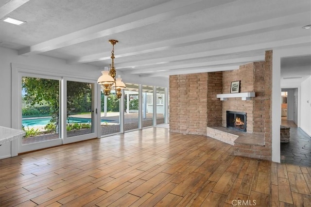 unfurnished living room featuring beamed ceiling, a textured ceiling, a brick fireplace, a notable chandelier, and hardwood / wood-style flooring