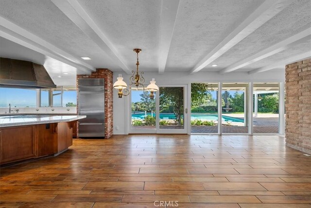 kitchen featuring hanging light fixtures, beam ceiling, a notable chandelier, ventilation hood, and stainless steel built in fridge