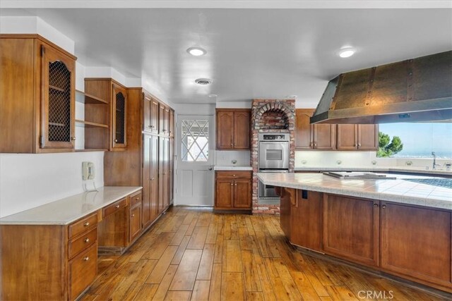 kitchen featuring ventilation hood, sink, decorative backsplash, hardwood / wood-style flooring, and stainless steel double oven