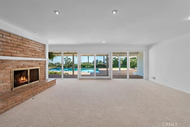 unfurnished living room featuring carpet floors, a brick fireplace, and a wealth of natural light