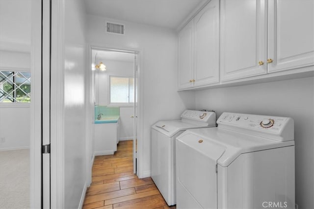 clothes washing area featuring light hardwood / wood-style flooring, sink, washer and clothes dryer, and cabinets