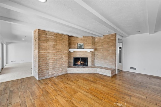 unfurnished living room with a brick fireplace, beam ceiling, and a textured ceiling