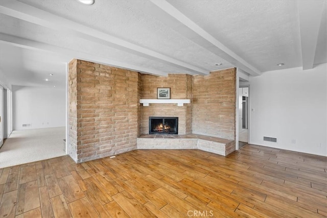 unfurnished living room with a textured ceiling, a brick fireplace, beamed ceiling, and hardwood / wood-style floors