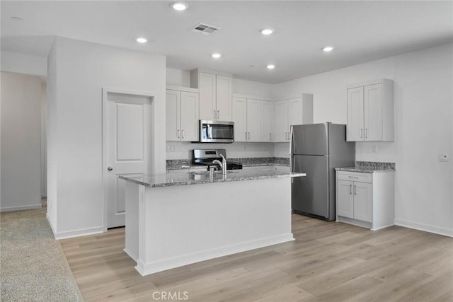 kitchen with white cabinets, appliances with stainless steel finishes, light hardwood / wood-style flooring, and an island with sink