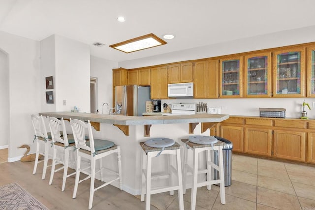 kitchen with a breakfast bar area, sink, light tile patterned floors, and white appliances