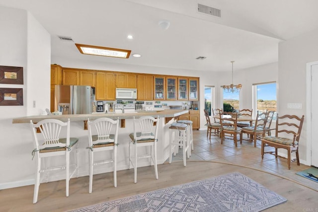 kitchen with white appliances, a kitchen breakfast bar, decorative light fixtures, light hardwood / wood-style flooring, and a notable chandelier