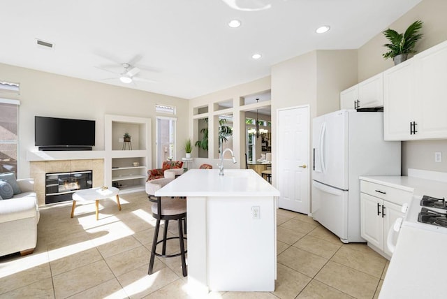 kitchen with a breakfast bar, white refrigerator with ice dispenser, an island with sink, white cabinetry, and light tile patterned flooring