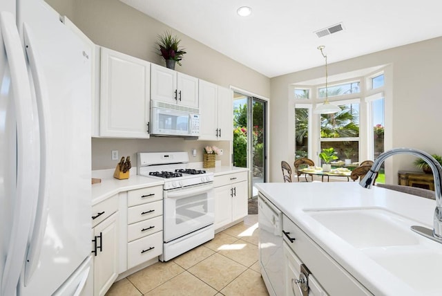 kitchen featuring white appliances, sink, hanging light fixtures, light tile patterned floors, and white cabinetry