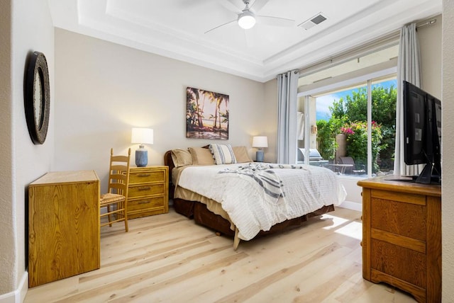 bedroom featuring ceiling fan, a tray ceiling, and light hardwood / wood-style flooring