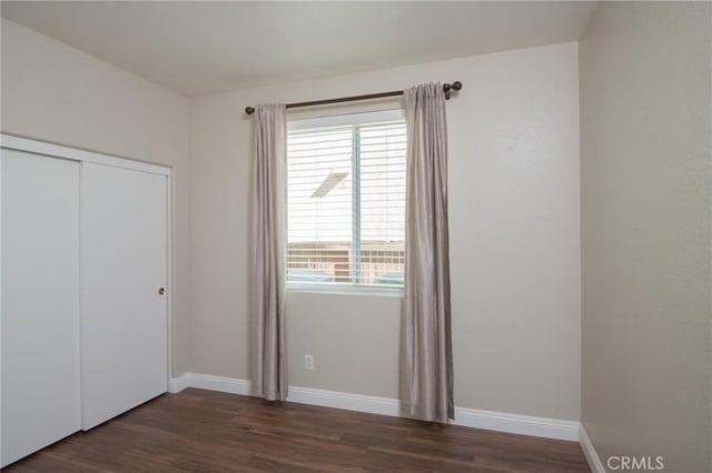 unfurnished bedroom with dark hardwood / wood-style flooring, a closet, and multiple windows