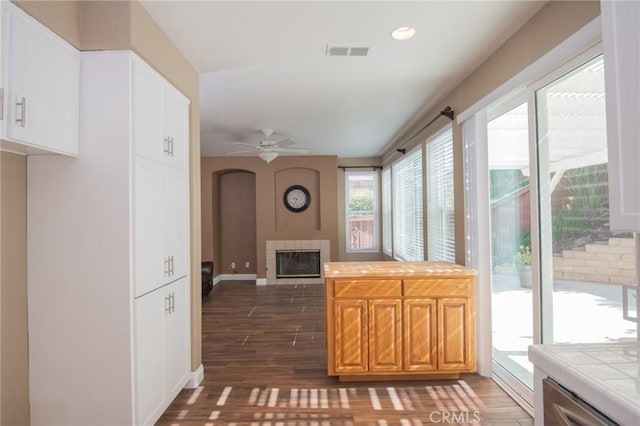 kitchen featuring a tile fireplace, tile countertops, ceiling fan, and dark wood-type flooring