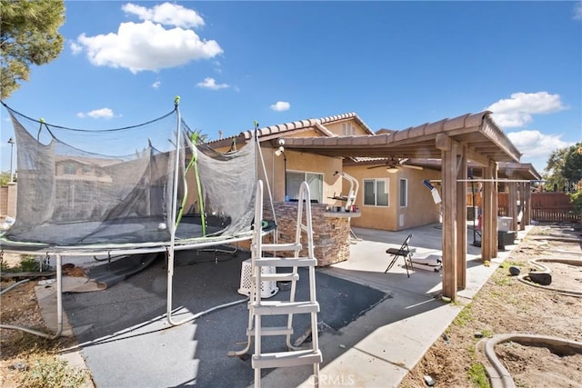 back of property featuring ceiling fan, a bar, a patio, and a trampoline