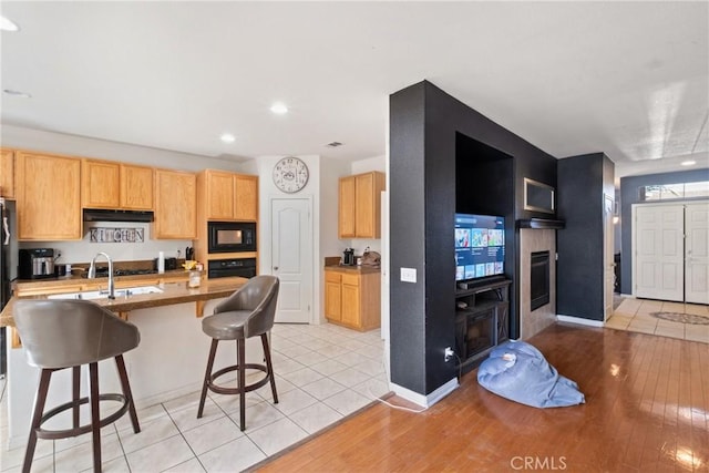 kitchen with a breakfast bar, light brown cabinets, black appliances, sink, and light hardwood / wood-style floors