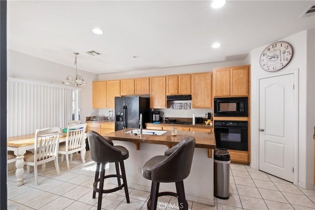 kitchen featuring sink, black appliances, light tile patterned floors, a notable chandelier, and an island with sink