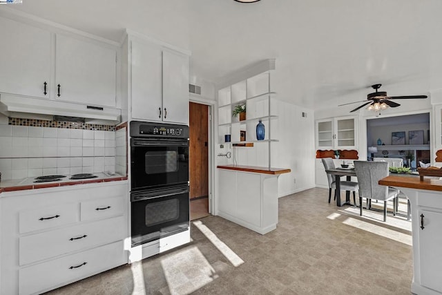 kitchen with backsplash, black double oven, white stovetop, white cabinets, and tile counters