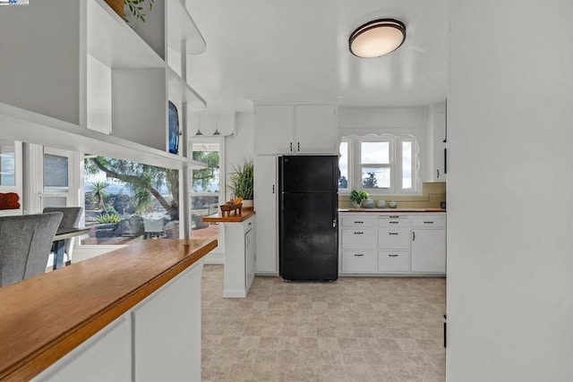 kitchen featuring white cabinets, black fridge, and a wealth of natural light