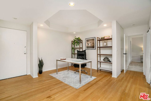 office area with a tray ceiling and light wood-type flooring