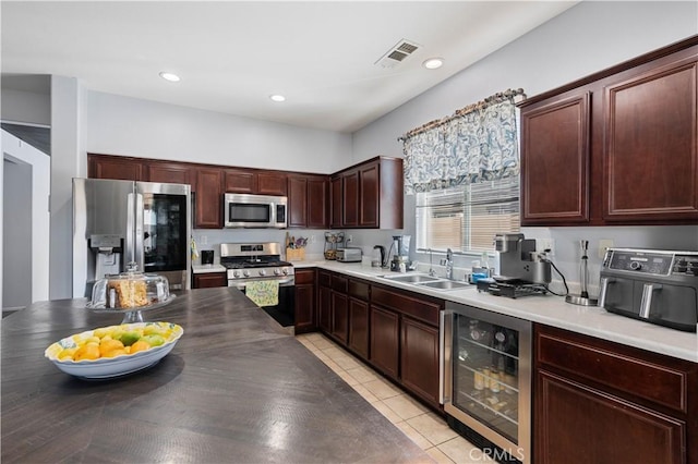 kitchen with appliances with stainless steel finishes, light tile patterned floors, sink, and beverage cooler