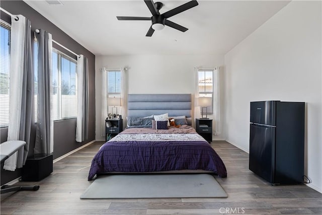 bedroom with ceiling fan, dark hardwood / wood-style flooring, and black fridge