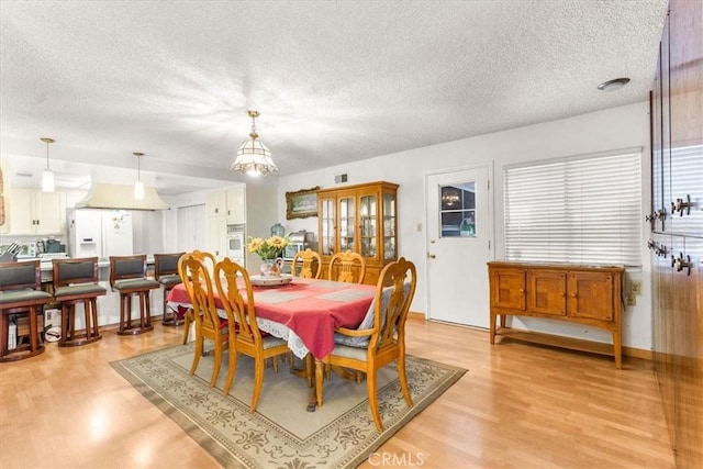 dining room with an inviting chandelier, a textured ceiling, and light wood-type flooring