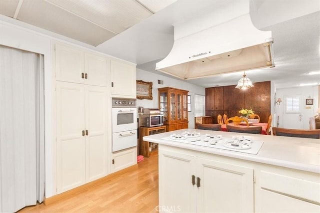 kitchen featuring white cabinets, light wood-type flooring, white appliances, and extractor fan