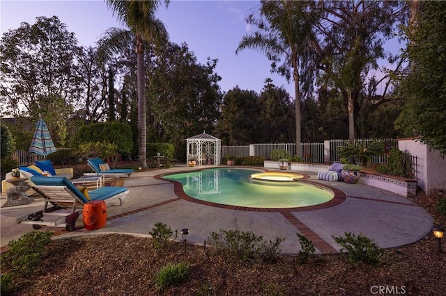 pool at dusk with a patio area and an in ground hot tub