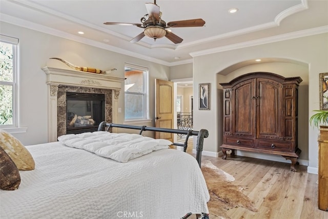 bedroom with a fireplace, ornamental molding, ceiling fan, a tray ceiling, and light hardwood / wood-style flooring