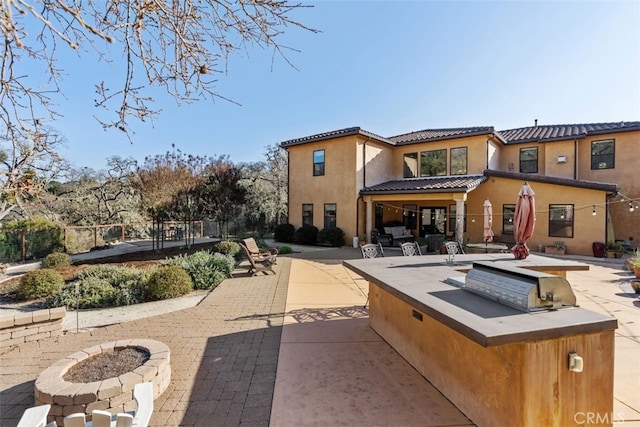 rear view of house featuring a fire pit, an outdoor kitchen, and a patio