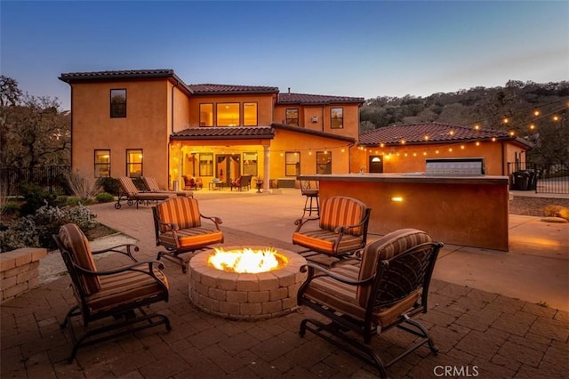 back house at dusk featuring a fire pit and a patio