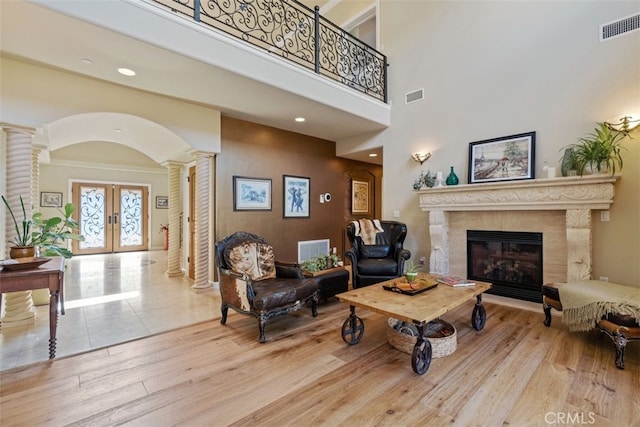 living room featuring a towering ceiling, ornate columns, light hardwood / wood-style floors, a fireplace, and french doors