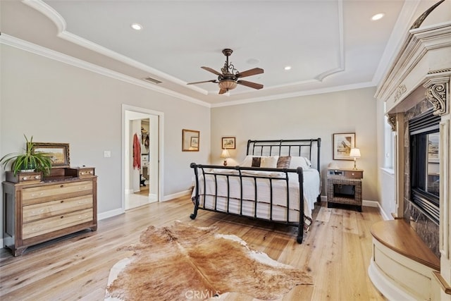 bedroom with a spacious closet, light hardwood / wood-style floors, a tray ceiling, and ceiling fan