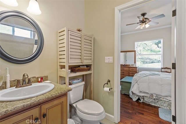 bathroom with wood-type flooring, ceiling fan, ornamental molding, toilet, and vanity