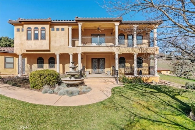 mediterranean / spanish-style house with a balcony, a front lawn, and french doors