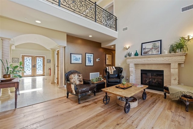 living room with ornate columns, light hardwood / wood-style floors, french doors, a high ceiling, and a premium fireplace