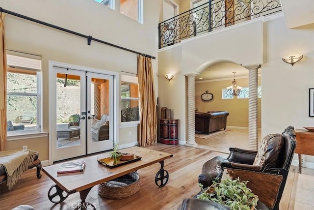 living room featuring crown molding, light wood-type flooring, a high ceiling, decorative columns, and an inviting chandelier