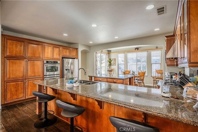 kitchen with light stone countertops, appliances with stainless steel finishes, dark hardwood / wood-style flooring, sink, and a breakfast bar area